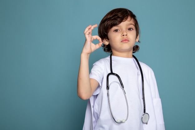 Mignon petit garçon enfant en combinaison médicale blanche montrant signe sur mur bleu