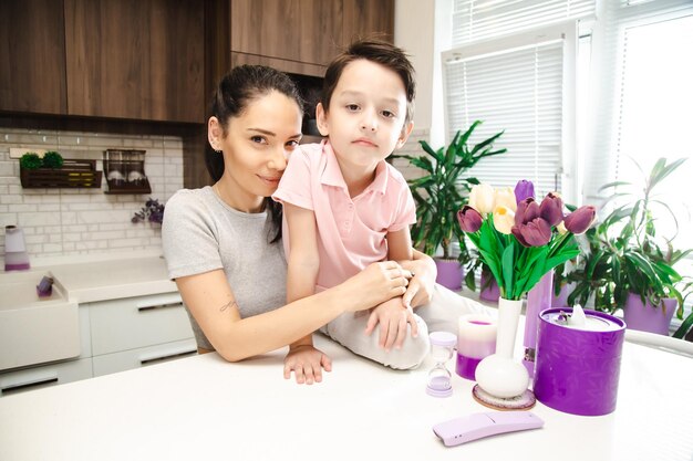 Mignon petit garçon avec une mère heureuse dans la cuisine lumineuse regardant la caméra avec des sourires sur les visages famille heureuse dans une cuisine à la maison