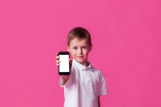 Mignon petit garçon montrant un téléphone portable à écran blanc sur fond rose