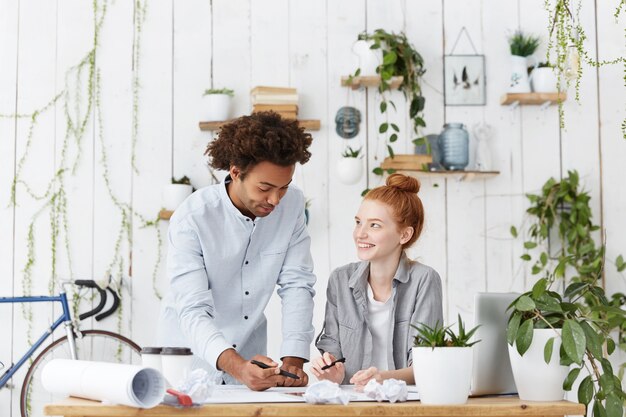 Mignonne jeune stagiaire rousse souriant tout en écoutant un architecte confiant qualifié