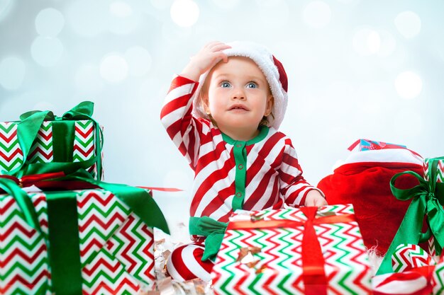Mignonne petite fille de 1 an portant bonnet de Noel posant sur des décorations de Noël avec des cadeaux. Assis sur le sol avec boule de Noël