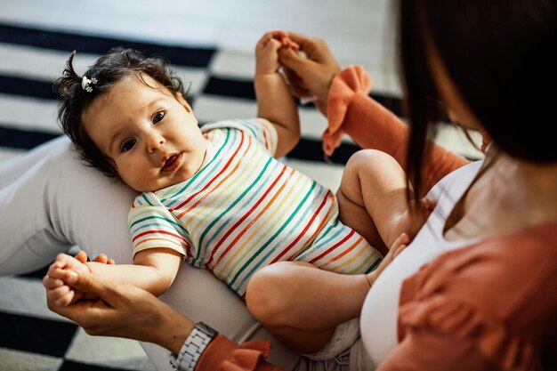 Mignonne petite fille allongée sur les genoux de sa mère tout en lui tenant les mains et en regardant la caméra