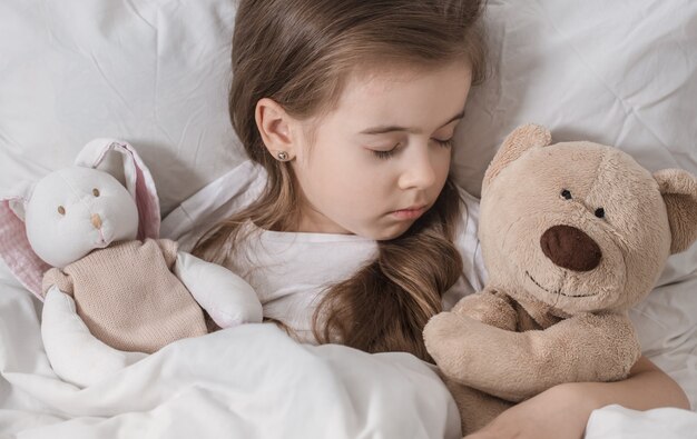 Mignonne petite fille au lit avec peluche.