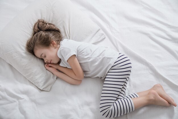 Mignonne petite fille aux cheveux longs qui dort dans son lit.