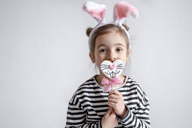 Mignonne petite fille avec du pain d'épice de Pâques sur un bâton et des oreilles de lapin décoratives sur sa tête.