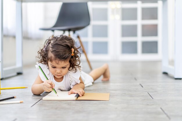 Mignonne petite fille écrivant sur un cahier allongé sur le sol