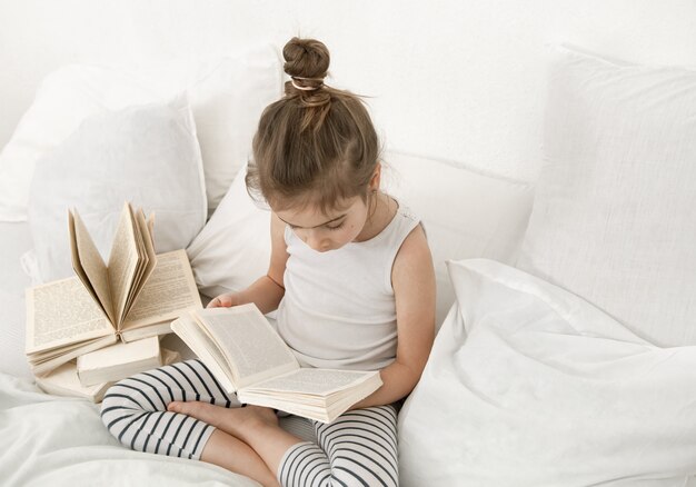 Mignonne petite fille lisant un livre sur le lit dans la chambre.
