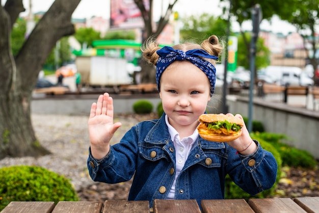 Mignonne petite fille a souligné le geste d'arrêt avec hamburger dans les mains avant de manger dans un café en plein air