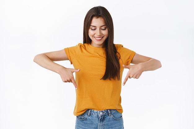 Mignonne tendre magnifique femme brune en t-shirt jaune regardant et pointant vers le haut debout amusée et se demandait d'observer un événement cool en vérifiant une bonne promo ou en participant à un cadeau génial