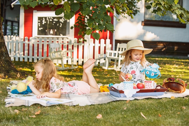 Mignonnes petites filles blondes lisant un livre à l'extérieur sur l'herbe