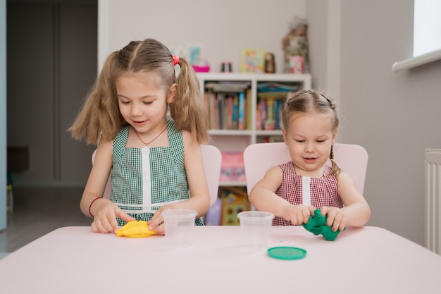 Mignonnes petites filles moulant de pâte à modeler sur table rose