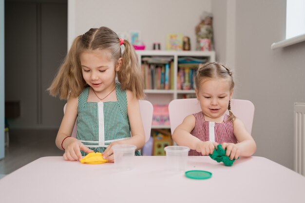 Mignonnes petites filles moulant de pâte à modeler sur table rose