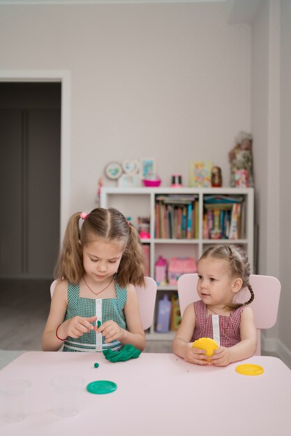 Mignonnes petites filles moulant de pâte à modeler sur table rose