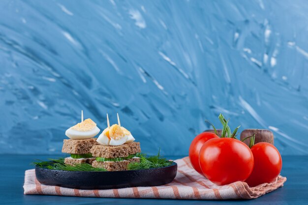 Mini brochette de sandwichs aux légumes et au fromage sur une planche sur un torchon, sur le fond bleu.