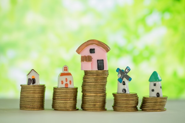 Mini maison sur pile de pièces avec flou vert.