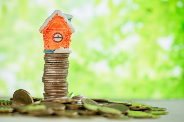 Mini maison sur pile de pièces avec flou vert.