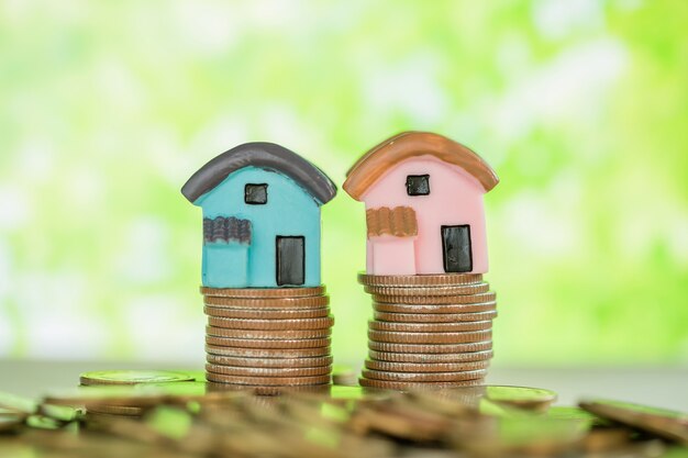 Mini maison sur pile de pièces avec flou vert.