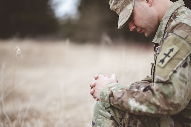 Mise au point peu profonde d'un jeune soldat priant à genoux sur une herbe sèche