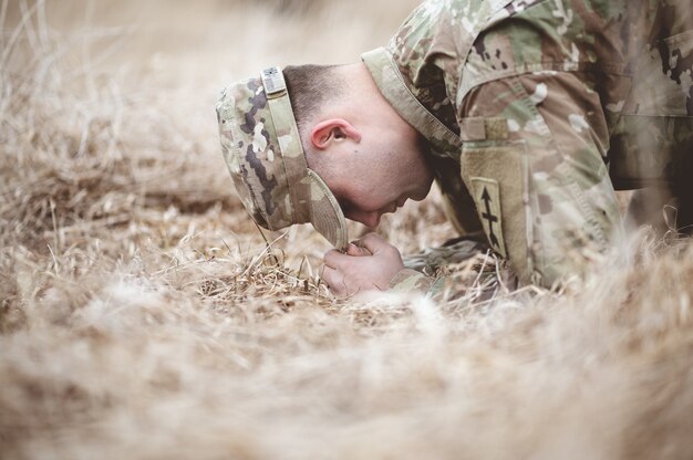 Mise au point peu profonde d'un soldat américain à genoux et priant sur un champ d'herbe sèche