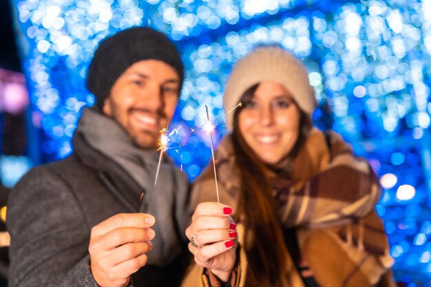 Mise au point sélective des feux de Bengale dans les mains d'un jeune et joyeux couple caucasien