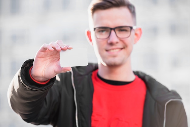 Photo gratuite mise au point sélective d'un jeune homme montrant une carte de visite vierge blanche