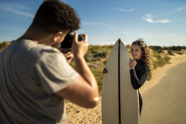 Mise au point sélective d'un photographe à prendre des photos d'une jolie femme tenant une planche de surf