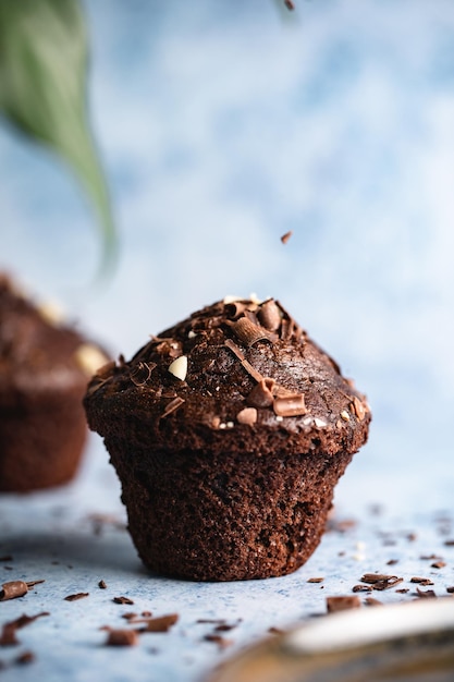 Mise au point sélective verticale de cupcakes au chocolat sur une surface bleue avec des pépites de chocolat tombant