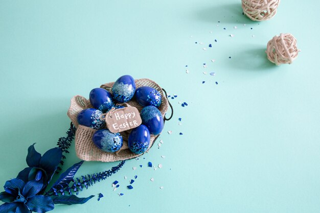 Mise en page créative de Pâques faite d'oeufs colorés et de fleurs sur fond bleu.