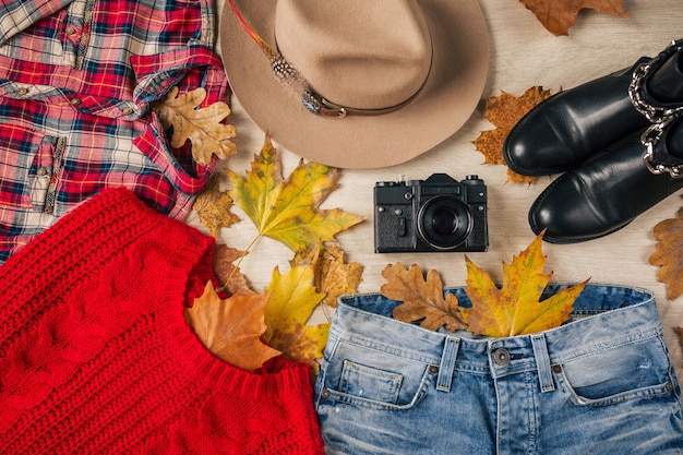Mise à plat du style femme et accessoires, pull en tricot rouge, chemise à carreaux, jean denim, bottes en cuir noir, chapeau, tendance de la mode automne, vue d'en haut, vêtements, feuilles jaunes