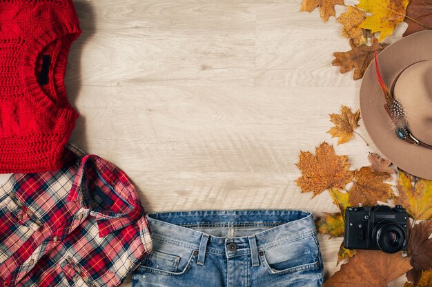 Mise à plat du style femme et accessoires, pull en tricot rouge, chemise à carreaux, jeans en denim, bottes en cuir noir, chapeau, tendance de la mode automne, vue d'en haut, appareil photo vintage, tenue de voyageur