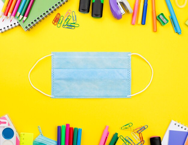 Mise à plat des éléments essentiels de l'école avec masque médical et crayons de couleur