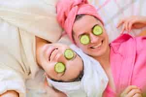 Photo gratuite mise à plat de femmes souriantes avec des tranches de concombre sur les yeux