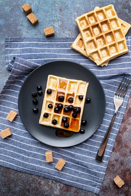 Mise à plat de gaufres couvertes de miel sur une plaque avec des fruits