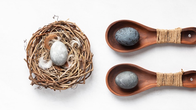 Mise à plat d'oeufs de Pâques dans le nid d'oiseau et cuillères en bois