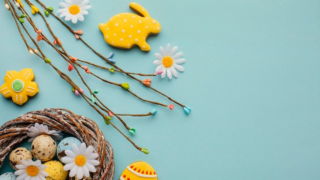 Photo gratuite mise à plat d'oeufs de pâques dans le panier avec des fleurs de camomille et lapin