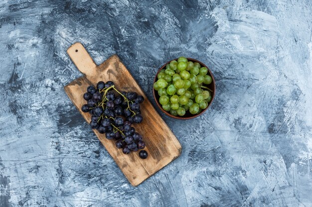 Mise à plat des raisins noirs sur une planche à découper avec bol de raisins blancs sur fond de marbre bleu foncé. horizontal