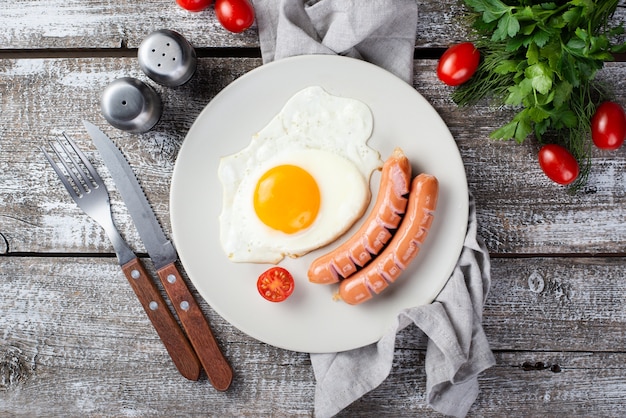 Mise à plat de saucisses de petit déjeuner et d'oeuf sur la plaque avec des tomates et des couverts