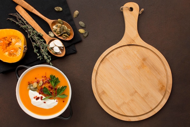 Photo gratuite mise à plat de la soupe de courge d'hiver dans un bol avec planche à découper et cuillères