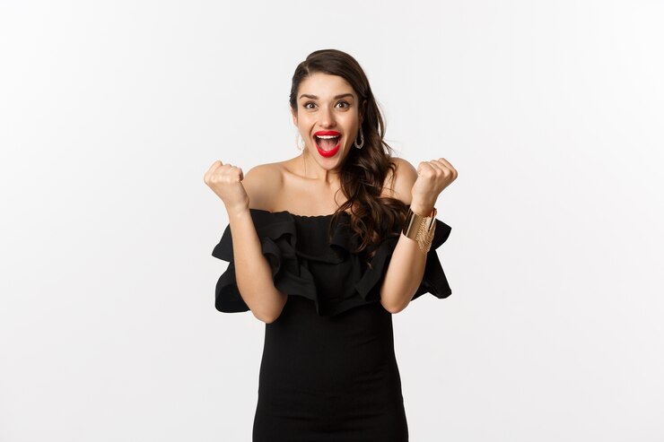 Photo gratuit mode et beauté. succès jolie femme en robe noire célébrant, se réjouissant de gagner, triomphant sur fond blanc.