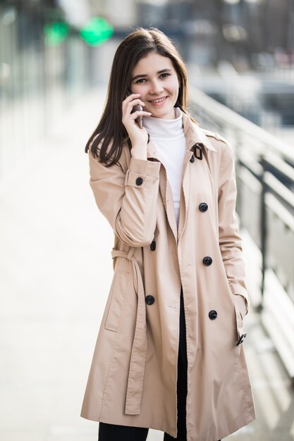 Mode femme en manteau marron clair marchant et parlant sur le téléphone mobile à l'extérieur