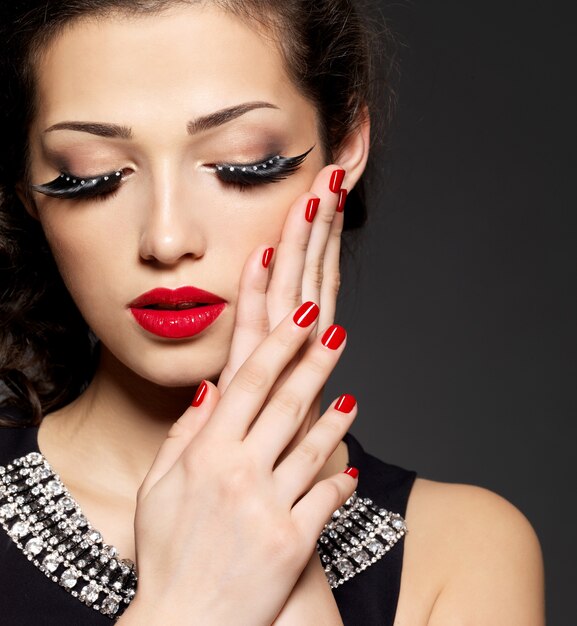 Mode femme avec maquillage créatif moderne à l'aide de faux cils manucure rouge