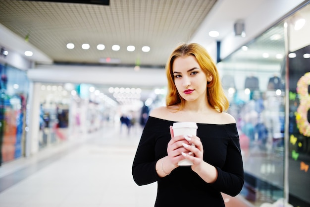 Photo gratuite mode fille aux cheveux rouges porter sur une robe noire avec un maquillage lumineux tenant une tasse de café au centre commercial commercial filtres instagram de style photo tonique