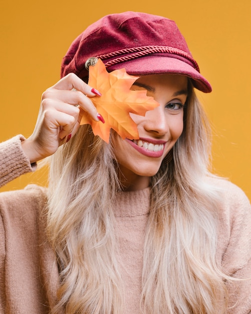 À la mode jeune femme portant casquette tenant une feuille d'érable en regardant la caméra