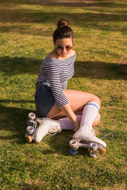 À la mode jeune femme portant des patins à roulettes assis sur l&#39;herbe verte