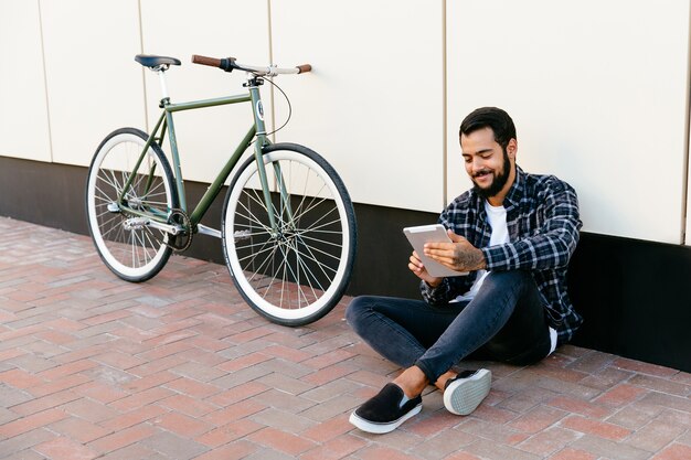 À la mode jeune homme barbu en utilisant une tablette numérique, souriant joyeusement