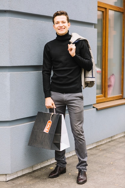 À la mode jeune homme avec des sacs à provisions tenant veste sur son épaule