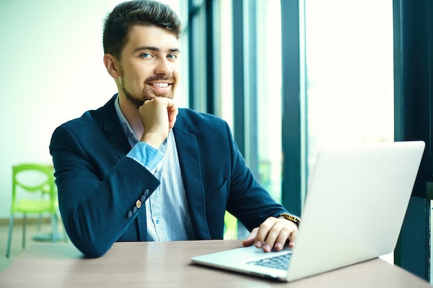 Mode jeune homme souriant hipster dans le café de la ville pendant l'heure du déjeuner avec un ordinateur portable en costume