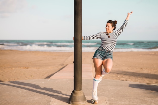 À la mode jeune patineuse tenant le pilier danser sur la plage