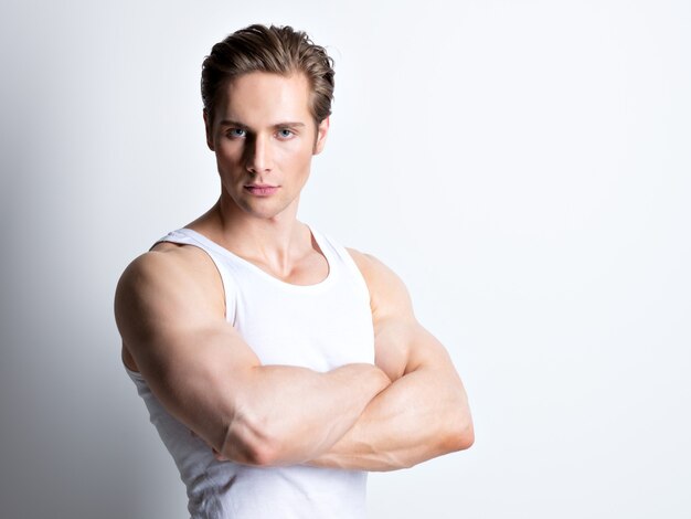 Mode portrait de beau jeune homme en chemise blanche avec les bras croisés pose sur le mur.