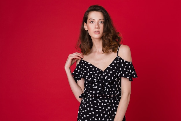 Mode portrait de la belle jeune femme en robe à pois noirs sur studio rouge